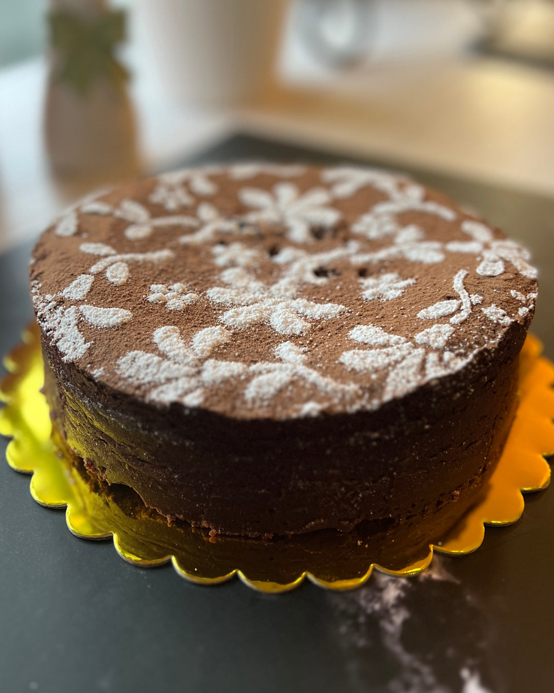 7inch flourless chocolate torte cake with powdered sugar on a yellow cake stand
